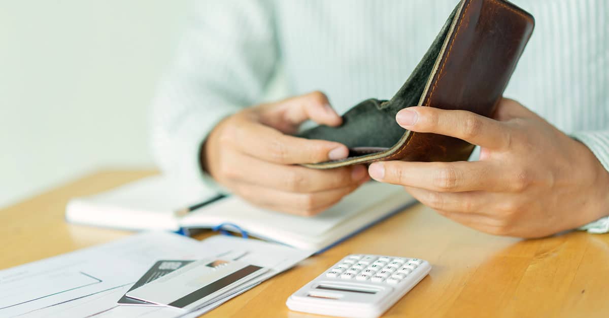 Hands holding an empty wallet with various stationery and a calculator on the desk. The image is used to imply that he is considering DIP financing.