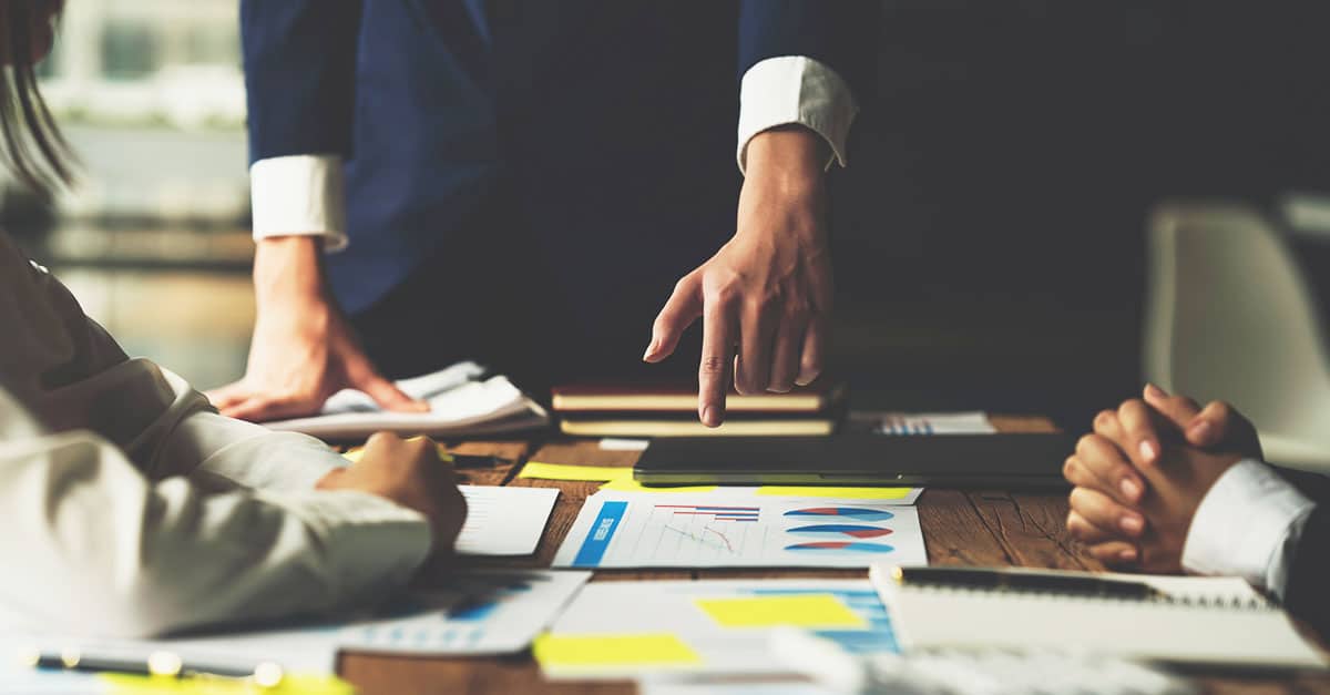 A team of three people on a table looking at charts and tables. The image is used to illustrate the process of procurement - either RFP or tender.